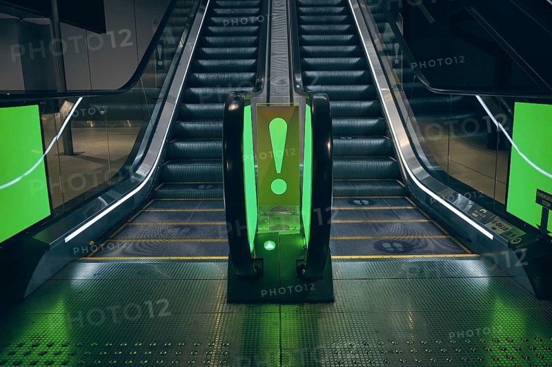 Empty escalator with exclamation mark and highlighted by green at airport terminal