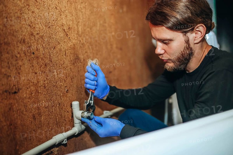 Person using a wrench on a pipe connection while wearing gloves