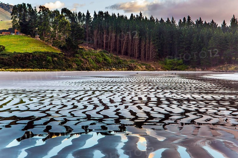 Sunrise over the ocean. Low tide. Strips of sand and water left by the ocean tide. The art of artistic photography. New Zealand, Pacific Coast. The concept of artistic photography. Artistic postal card