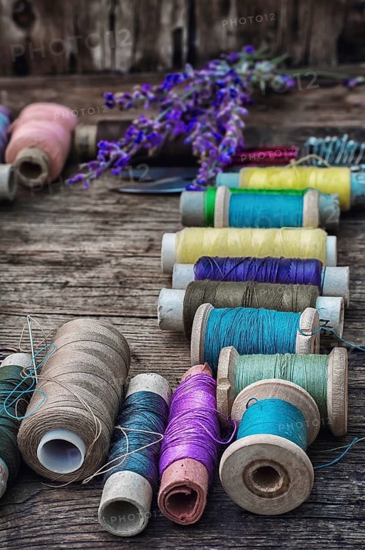 Spools of thread on the old wooden background decorated with branches blossoming lavender.selective focus