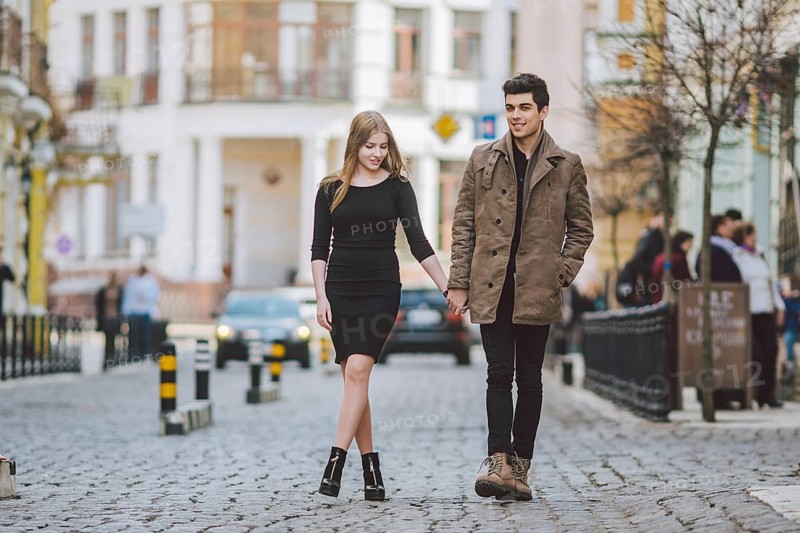 Urban modern young love couple walking romantic talking talking, holding hands on a date. Young multicultural Turkish brunette and Caucasian couple on old european street. Autumn spring weather