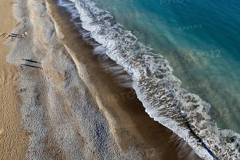 Aerial drone point of view of person walking on sand in a beach. Stormy waves idyllic beach in winter