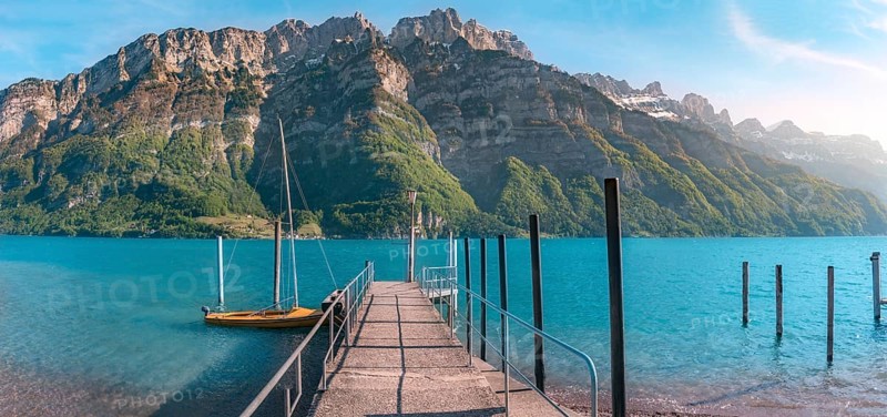 Spring landscape with a pier on the Walensee lake leading toward the Alps mountains, in Switzerland, on a sunny day of spring