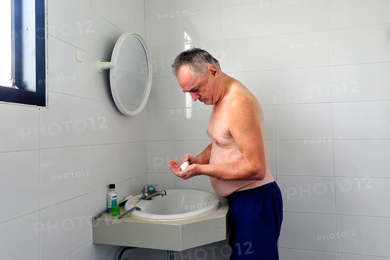 Man 60 plus shaves wet in the bathroom