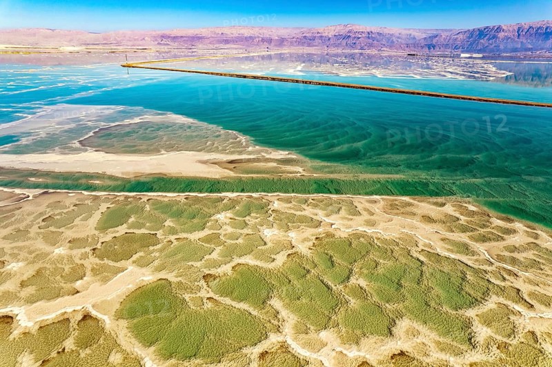 Salt deposits are visible on the seabed. Magic of the Dead Sea. The clear green water of the salty sea is surrounded by pink mountains. The photo was taken from a drone. Cold sunny day. Israel