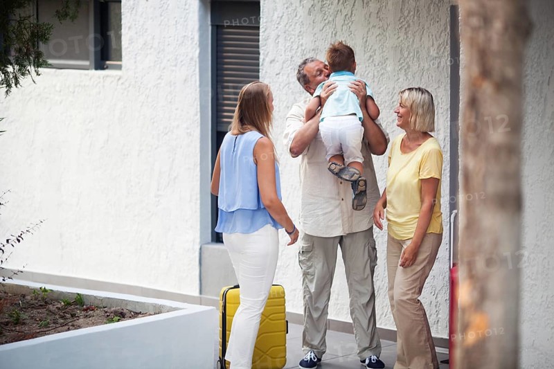 Grandfather greeting his young grandchild lifting him in the air and kissing him as he arrives on a trip with his mother outside the apartment