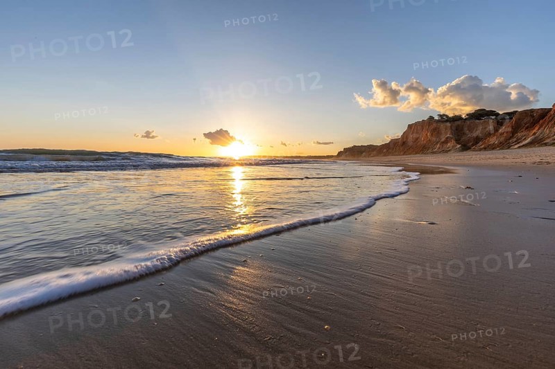 Beautiful sandy beach with red rocks and cliffs. Twilight at sunset with shallow waves on the Atlantic coast in Praia do Poço Velho, Praia da Falésia, Algarve, Portugal, Europe