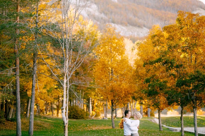 Portrait of smiling man hugging woman with wreath of yellow leaves in autumn forest.