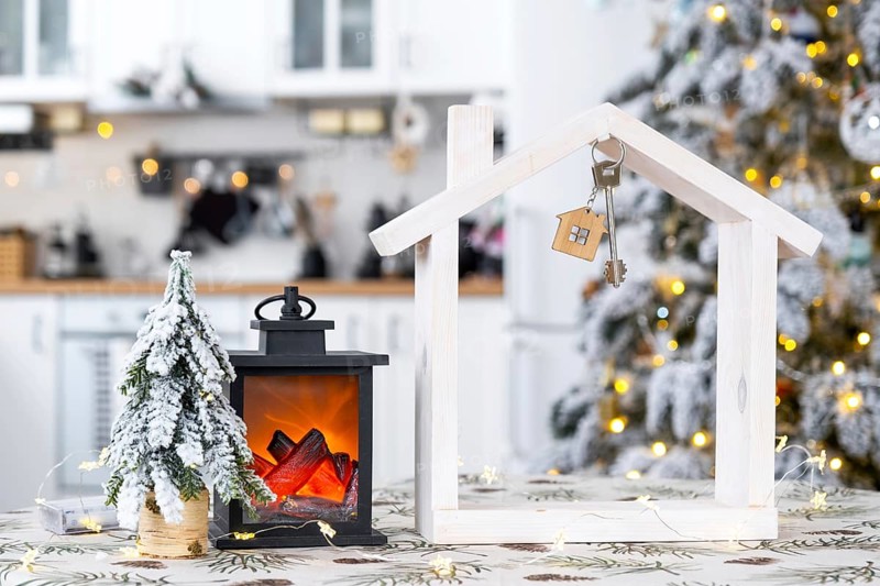 Key and tiny house of a small size on cozy home with Christmas decor on table of festive white kitchen. Gift for New Year. Insurance, moving to new house, mortgage, rent and purchase real estate