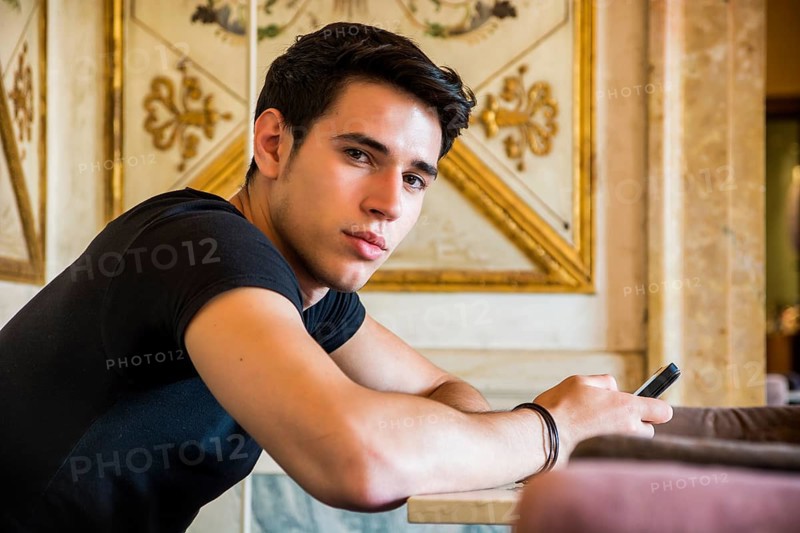 Young handsome man sitting in elegant cafeteria or restaurant using cell phone to send text message