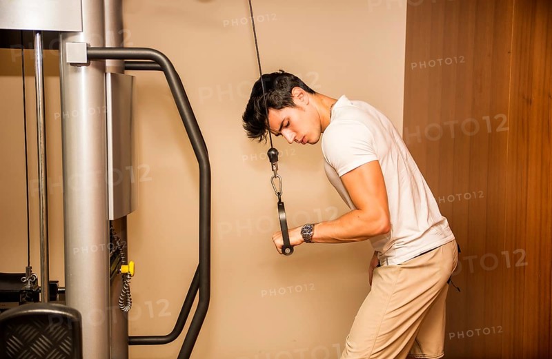 Attractive and fit young man in gym working out, doing pulley and exercising triceps on equipment