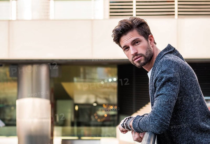One attractive man in urban environment in city, leaning on handrail, wearing cardigan