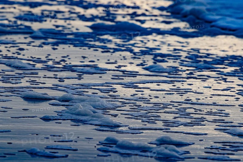 The sea waves and foam form textured patterns on the beach at dusk, Groede, Zeeland, Netherlands