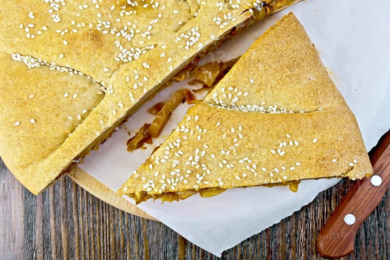 Pie with cabbage and sesame seeds with fresh rye dough knife on background wooden plank on top