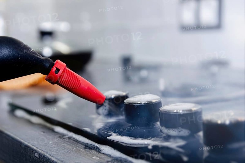 Close-up of a steam cleaner nozzle cleaning a stovetop