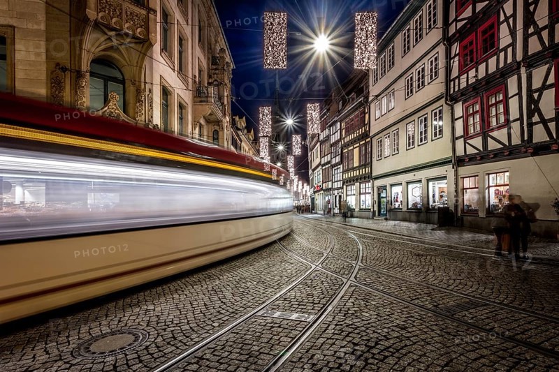 Langzeitbelichtung einer Straßenbahn, die durch eine historische Straße mit Fachwerkhäusern fährt, Erfurter Weihnachtsmarkt Erfurt