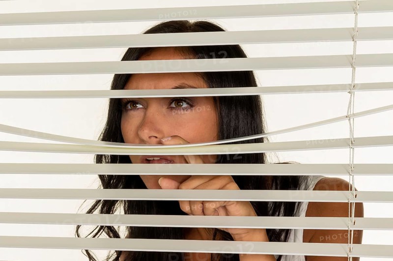 A young woman watches something through the blinds of her window Austria