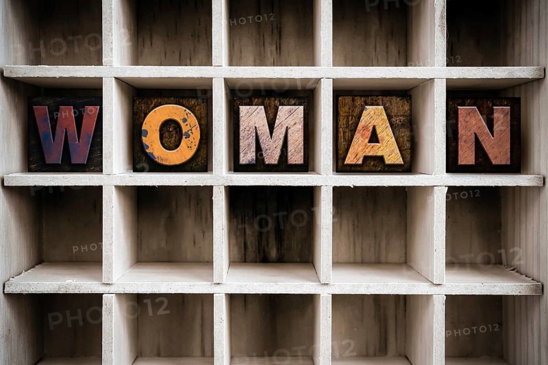 The word WOMAN written in vintage ink stained wooden letterpress type in a partitioned printer's drawer