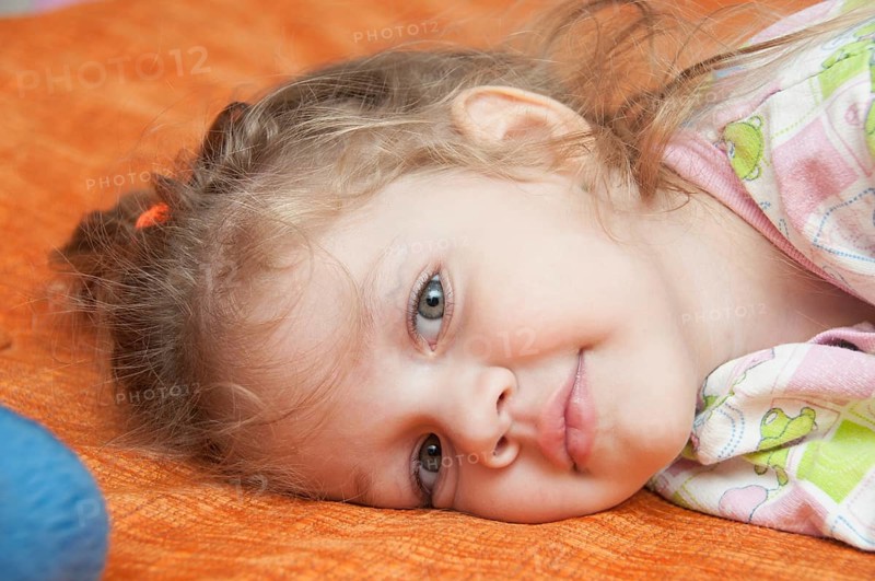 Cheerful three year old girl lying on the bed and looked into the frame