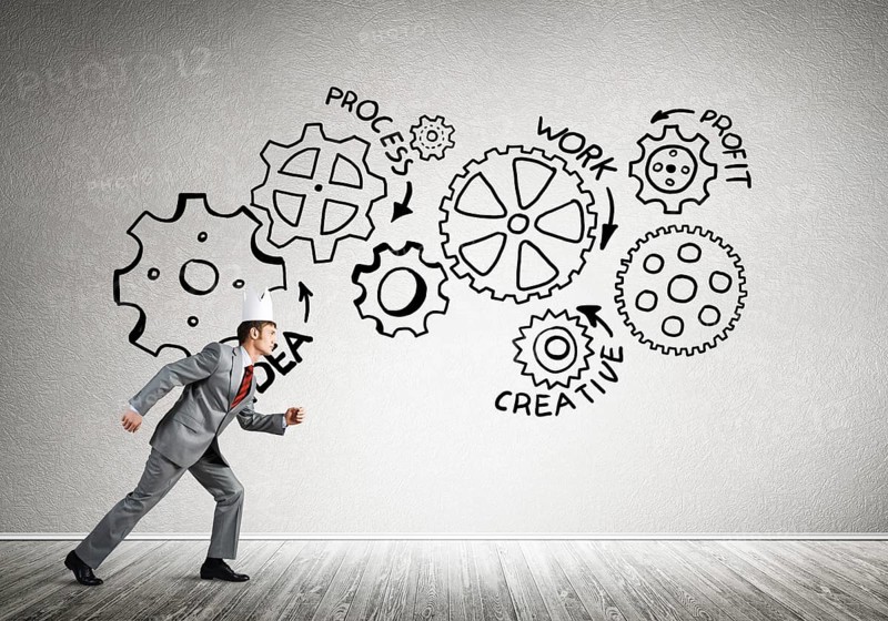 Young handsome businessman wearing white paper crown running and gear mechanism on wall