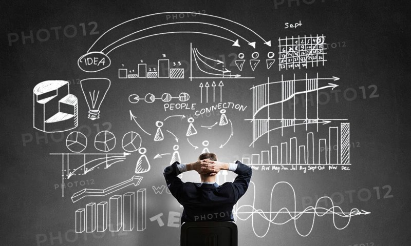 Rear view of businessman sitting in office chair and looking at infographs on chalkboard