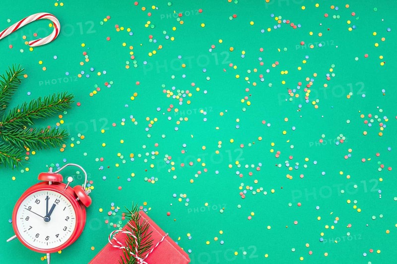 New Year or Christmas pattern flat lay top view with red alarm clock twelve midnight fir tree branch Xmas holiday celebration green paper bright colorful confetti background. Template text design 2019