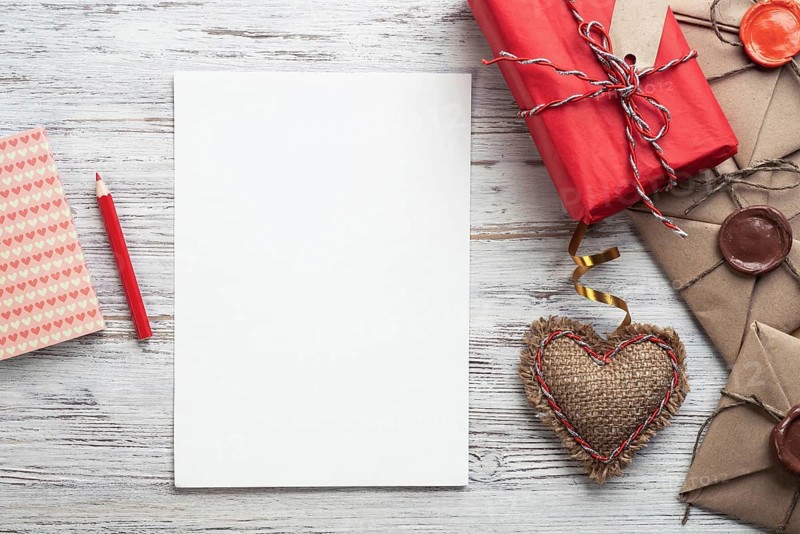 Flat lay composition with handmade fabric heart and gift box. Blank sheet of white paper on wooden surface. Romantic Saint Valentine's day congratulation. Baby born card. Wedding event invitation
