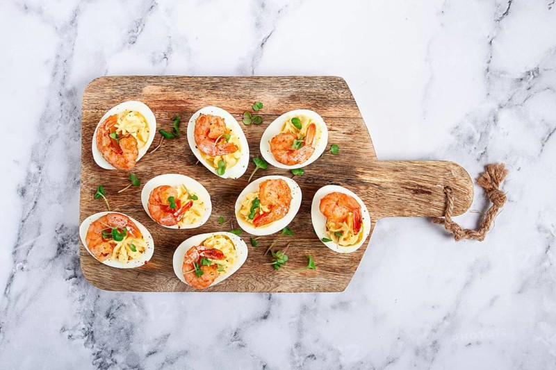 Boiled eggs stuffed with yolk and seasoned with mayonnaise, stuffed eggs with shrimp, on a wooden chopping board, selective focus, close-up, no people