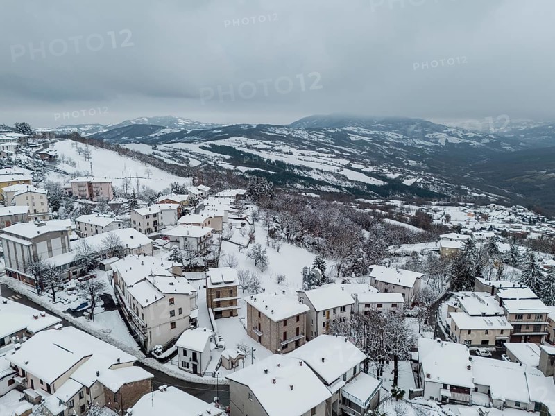 Aerial view of snow-covered houses and trees in bore, a small village nestled in the hills surrounding parma, italy, during a winter snowfall in december 2024