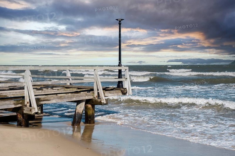 Storm sea waves empty wooden pier in dramatic blue sky background. Seascape with running splashing sea waves. Sandy beach vacation getaway in Gdansk Poland. Copy space for your text