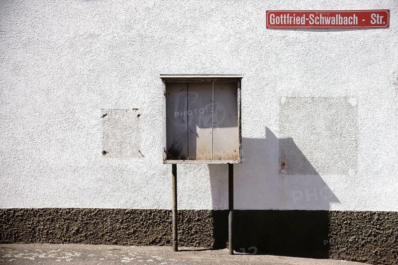 A vintage wooden display case stands on the façade of a building on the wall of which a cigarette machine and wooden frame have been dismantled
