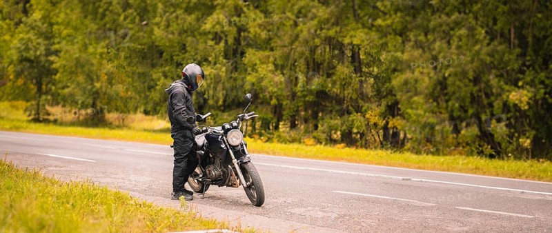 Motorcyclist checking their phone on a roadside near a forest