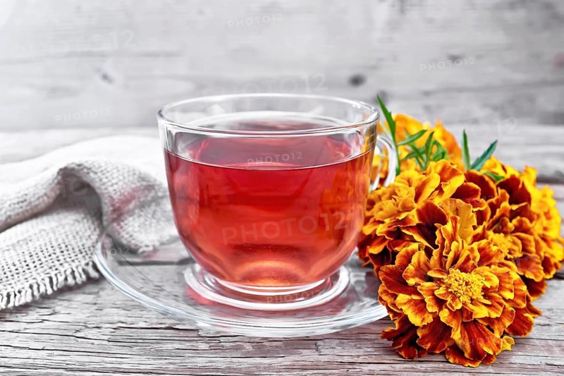 Marigold herbal tea in a glass cup and saucer, fresh flowers, burlap on wooden board background