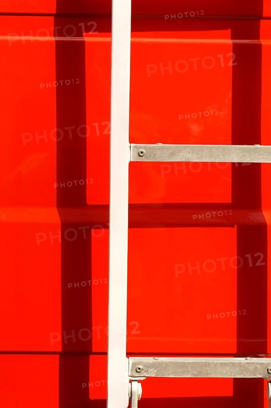 Close-up of the body of a fire engine in the sunshine with a ladder casting a shadow