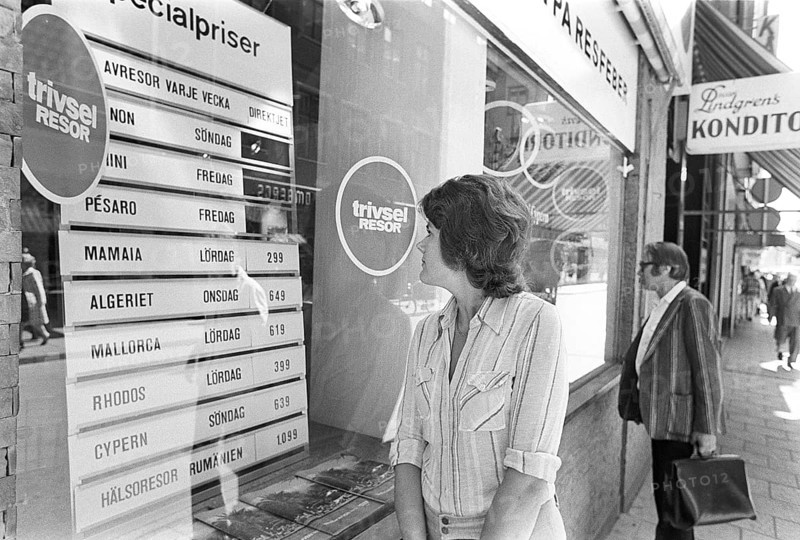 In the shop window of a travel agency. A woman is seen looking at the sign and information of the special prices for charter and package holidays to different destinations in the sunny part of south of Europe. 1975 Kristoffersson ref DV21