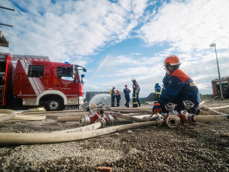 Fire engine and firefighters training, surrounded by hoses under a blue sky