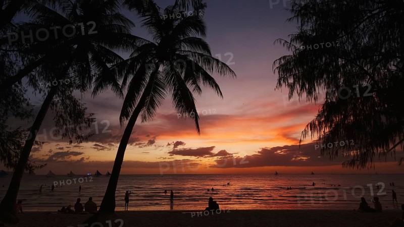 Silhouetted people and palms near sea. Sunset at tropical White beach, Boracay island, Philippines, Asia