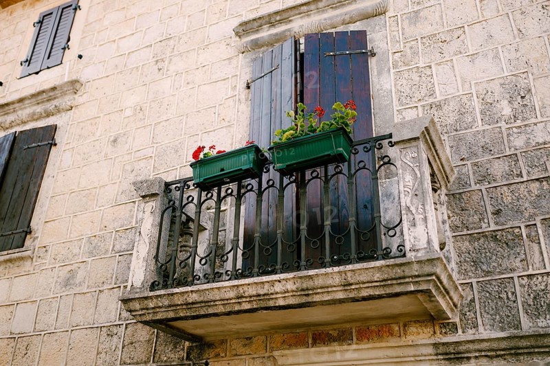 Stone balcony with a wrought iron lattice with flowerpots on the stone facade of the house.