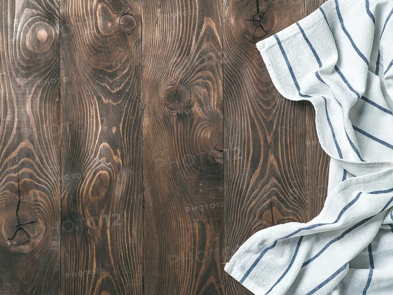 View from above on brown wooden table with linen kitchen towel or textile napkin. Blue tablecloth on dark brown wood tabletop. Copy space for text. Can use as mock up for design