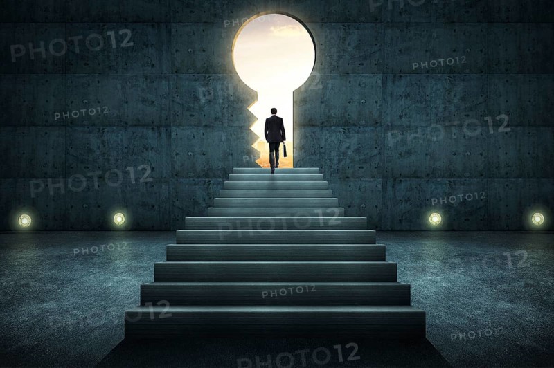 Sucess businessman climbing on stair against conrete wall with key hole door, sunrise scene city skyline outdoor view
