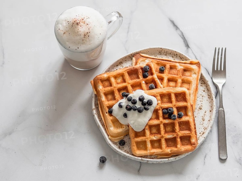 Delicious homemade baked belgian waffles with greek yogurt, blueberries and cappuccino on white marble background. Perfect breakfast with copy space for text or design. Top view or flat lay