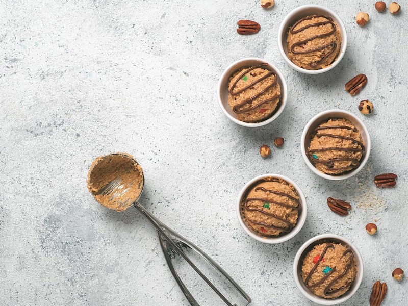 Safe-to-eat raw monster cookie dough in small portion bowl, ice cream scoop and nuts on gray cement background. Ideas and recipes for kids and toddlers meal. Top view or flat-lay. Copy space for text