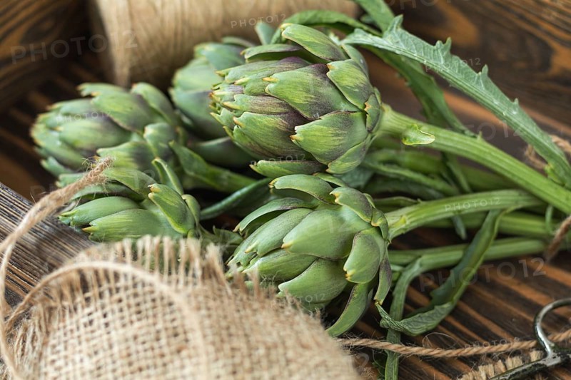 Two artichoke bouquets on kitchen table among some kitchen items. Top view