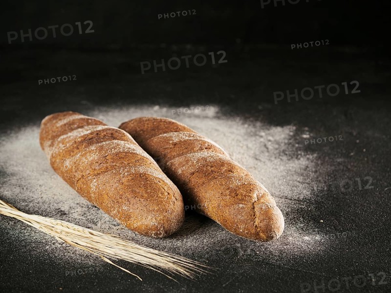 Two whole homemade rye loaf bread with buckwheat flour on black textured background. Copy space. Low key