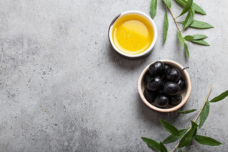 Black olives and extra virgin olive oil in little bowl with olive tree branches top view on gray concrete stone background, space for text, food photography, food photography