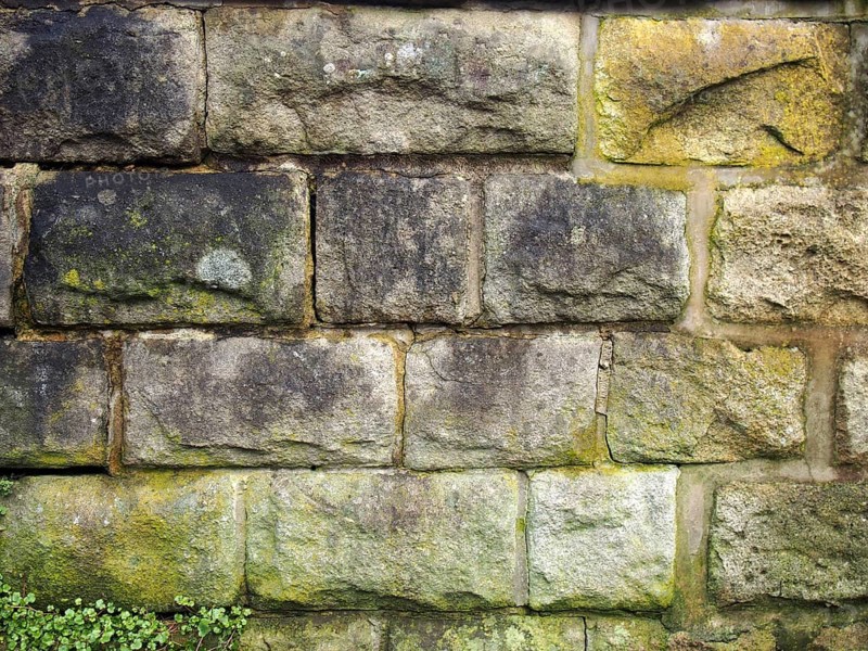 An old grey damp stone wall made of large regular blocks covered in patches of moss