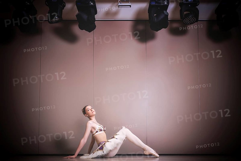 Young beautiful graceful caucasian ballerina practice ballet positions in tutu skirt. Classical Ballet dancer sitting on the floor in the studio