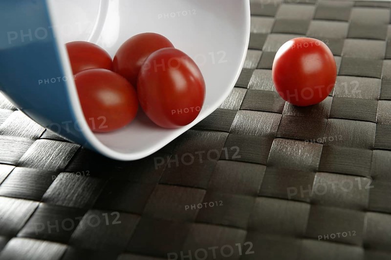 Group of cherry tomatoes falling from blue bowl over brown tablacloth