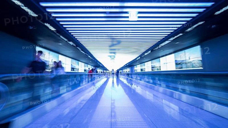 People going in walkway and riding flat escalators at the airport of Seoul, South Korea. Futuristic blue toned shot