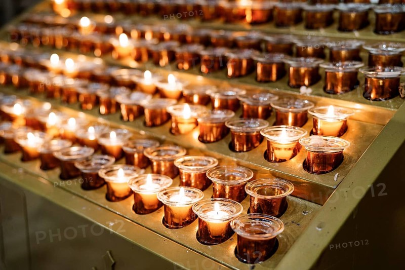 Votive candles burn in rows on a stand in the temple. Close-up.